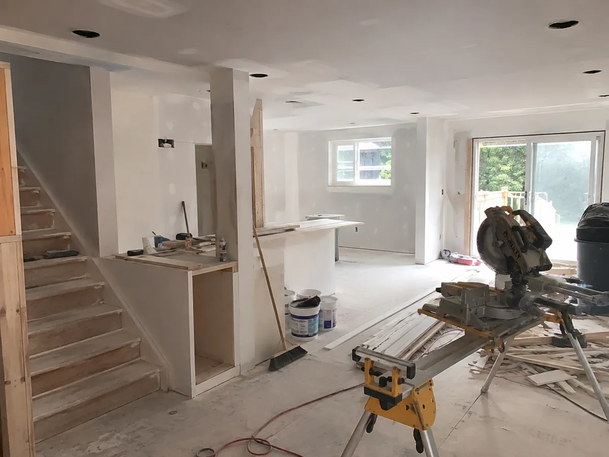 Open-concept main floor renovation in progress with drywall, kitchen island framing, and mitre saw in an Ottawa home